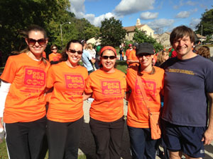 Four women and a man wrap arms around each other and smile for a photograph wearing orange Joe's Run T-shirts